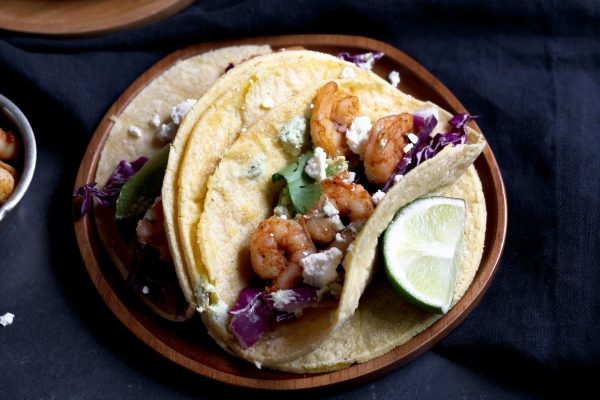 Shrimp tacos on a wooden plate with lime wedges.