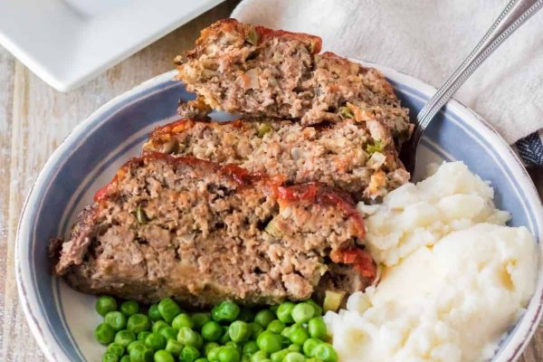 Meatloaf in a bowl with peas and mashed potatoes.
