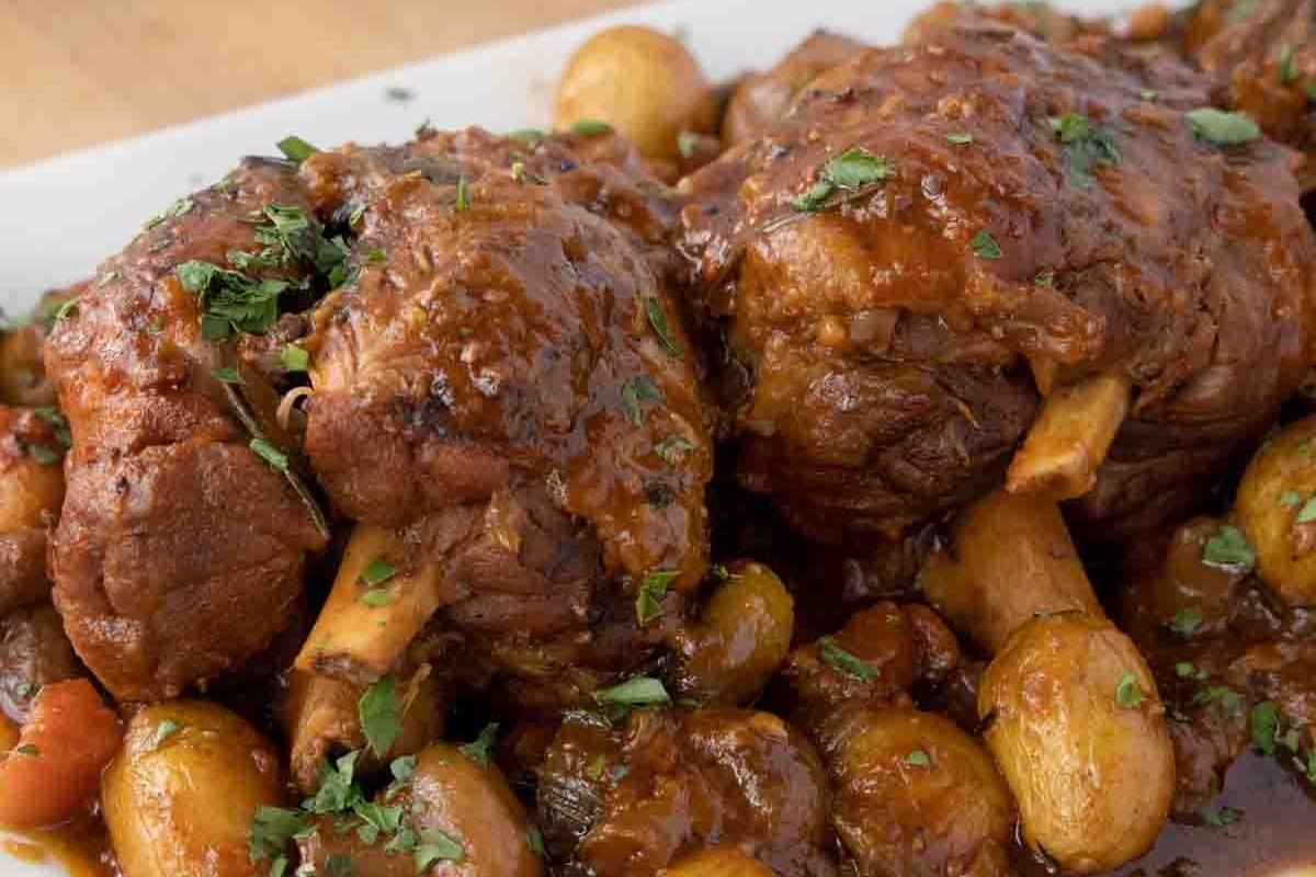 A plate of lamb and potatoes with gravy on it.