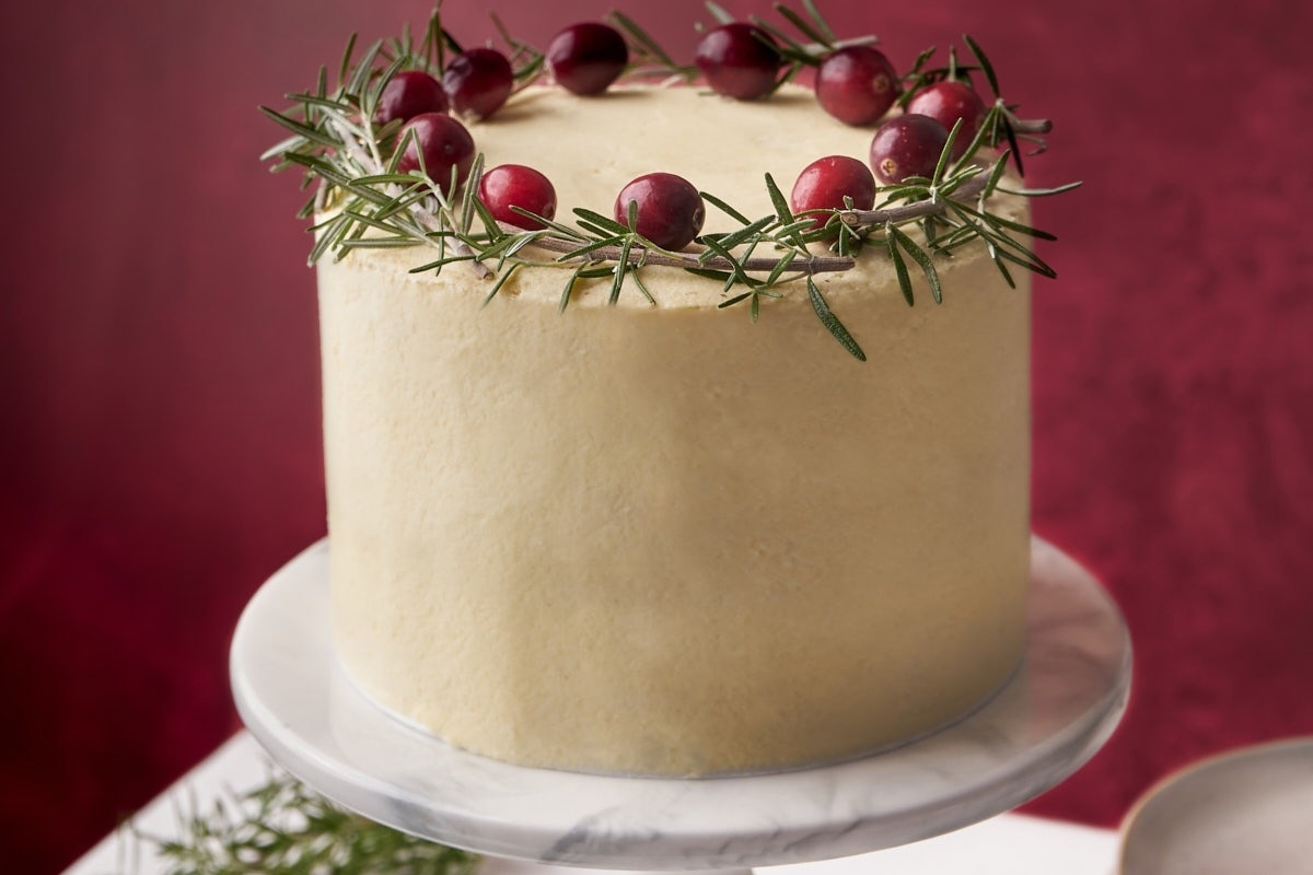 A Christmas cake decorated with cranberries and sprigs of rosemary.