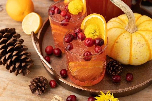 A tray of drinks with oranges, cranberries and pine cones.