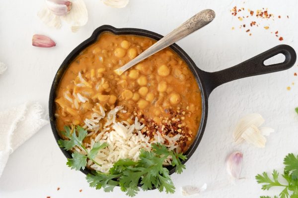 Chickpea curry recipe using pantry staples cooked in a skillet on a white background.