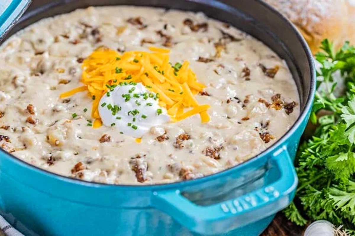 Cheesy potato soup in a blue pot with sour cream and parsley.