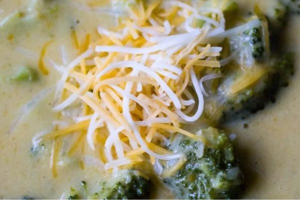 A creamy bowl of broccoli soup with cheese on top.