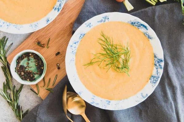 A creamy bowl of carrot soup with herbs on a table.
