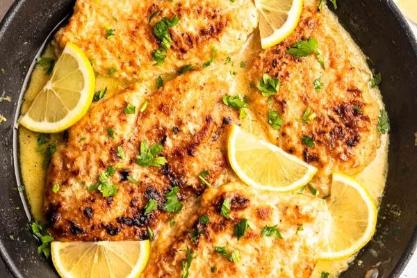 Chicken breasts in lemon sauce in a skillet.