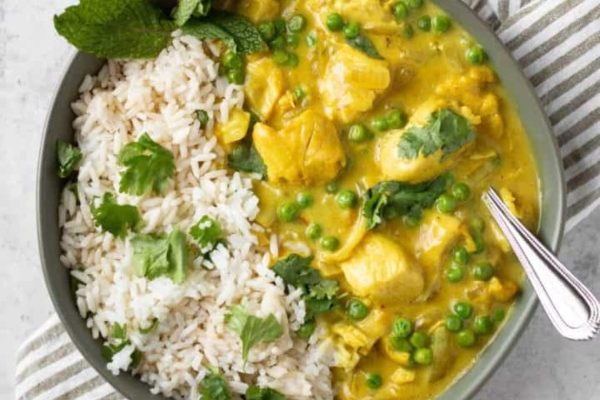 A bowl of chicken curry with rice and peas.