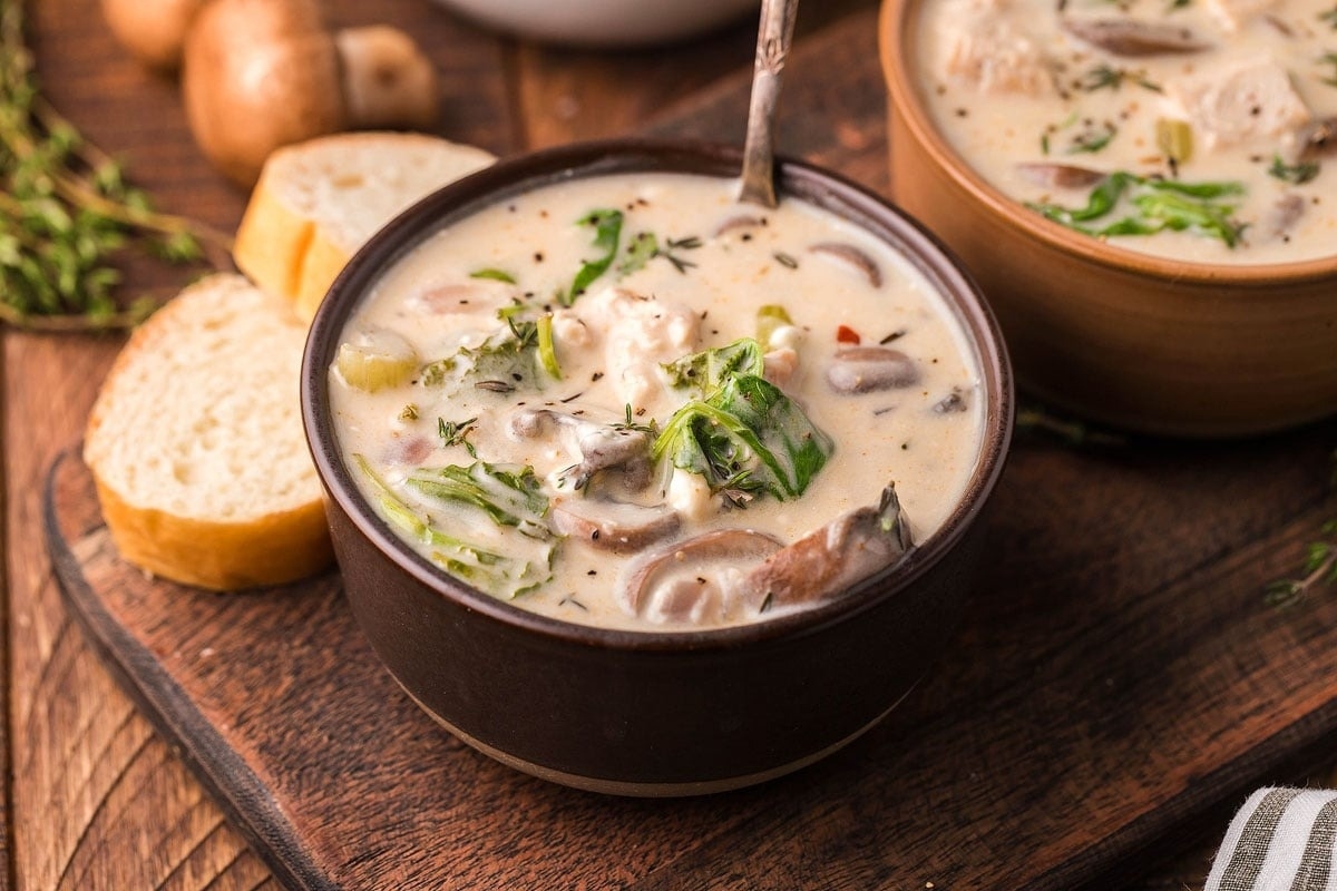 Two bowls of leftover turkey soup with mushrooms and bread on a wooden table.