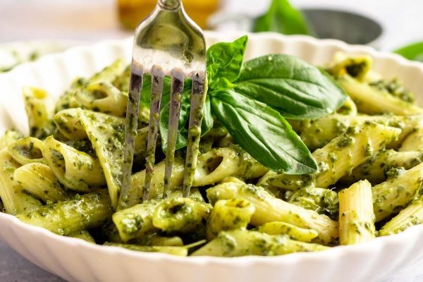Pesto pasta in a white bowl with a fork.