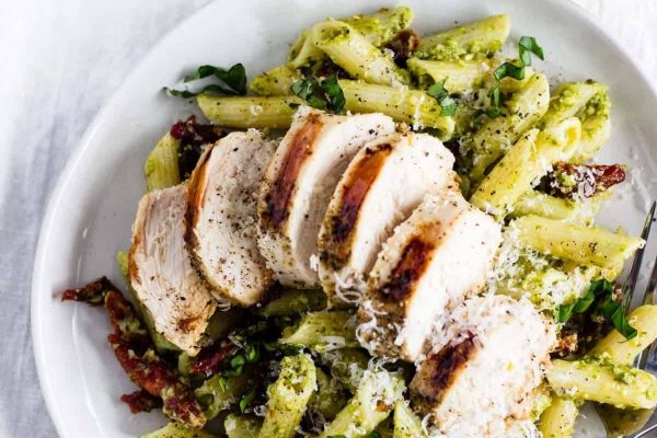 A white plate with chicken and pesto Penne pasta.