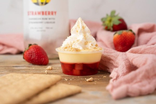 A cup with whipped cream and strawberries next to a bottle of vodka. This recipe is perfect for making delicious Jello shots!
