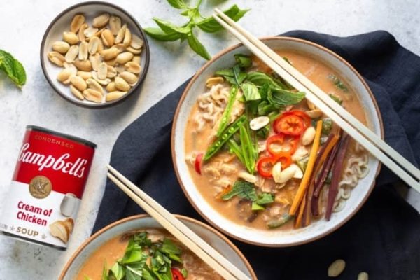 Two bowls of noodle soup with chopsticks next to a can of campbell soup.