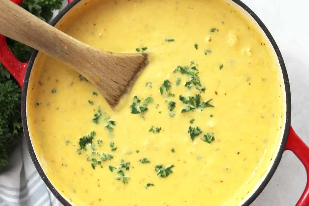Cheesy broccoli soup in a red pot with a wooden spoon, perfect for leftover turkey recipes.