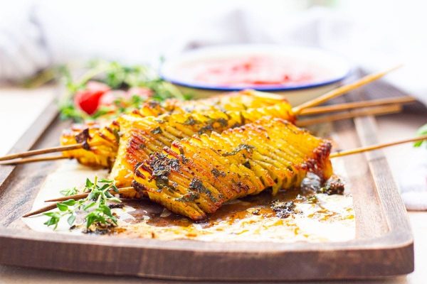 Skewered vegetables on a wooden board with dipping sauce.