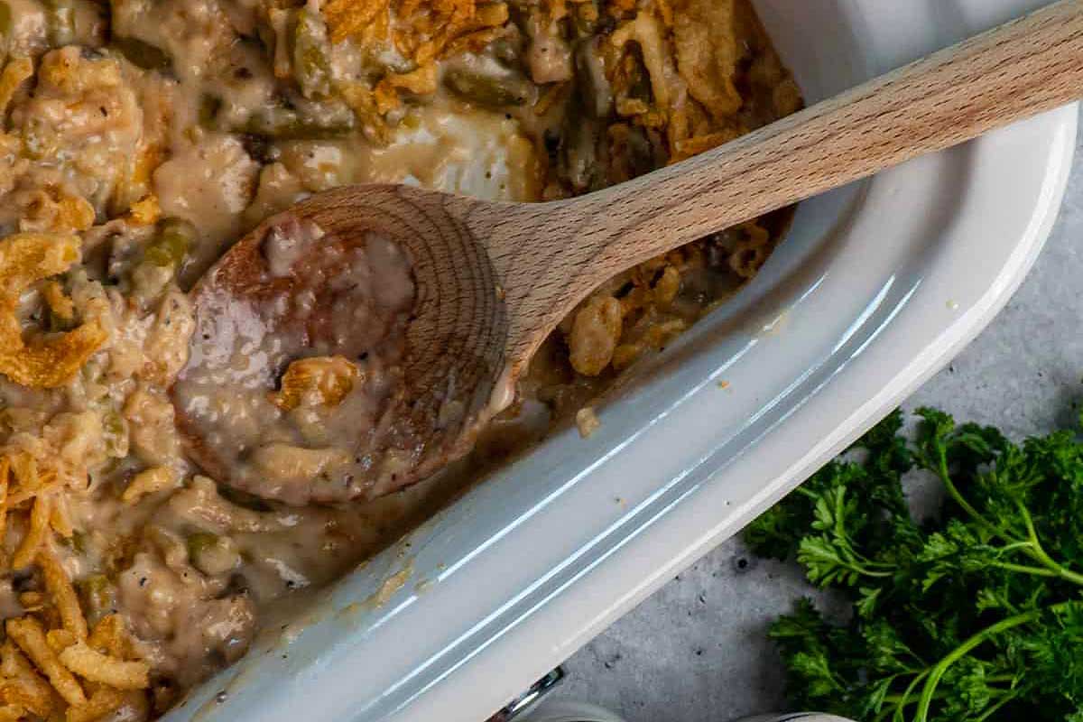 A casserole dish with a wooden spoon and green beans.