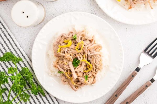 Pork tenderloin on a white plate with lemons and parsley.