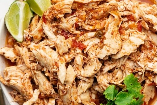 Shredded chicken in a white bowl with lime and cilantro.