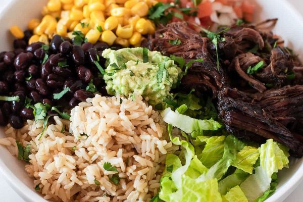 A bowl of rice, beans, corn and meat in a white bowl.
