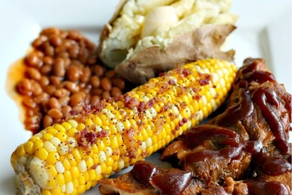 Bbq ribs, corn, potatoes and beans on a white plate.