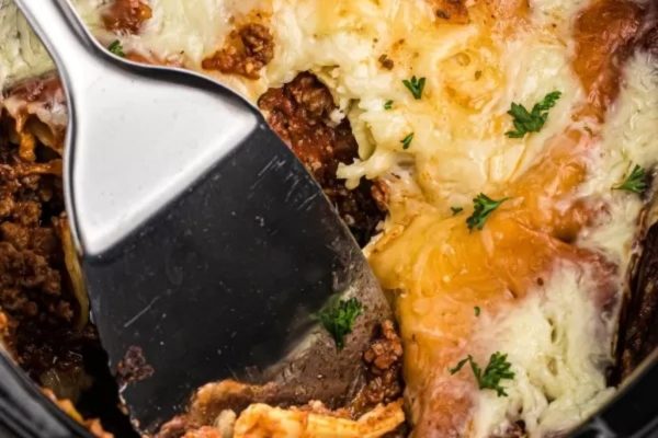 A spoon is taken out of a crock pot full of lasagna.
