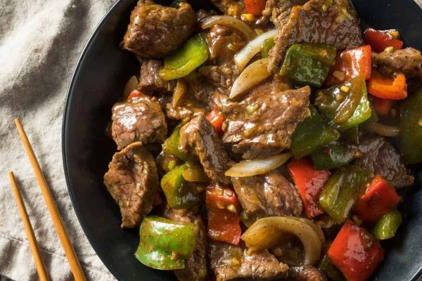 Beef stir fry in a black bowl with chopsticks.