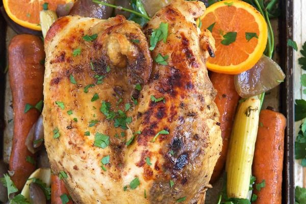 Roasted chicken with carrots and oranges on a baking sheet.