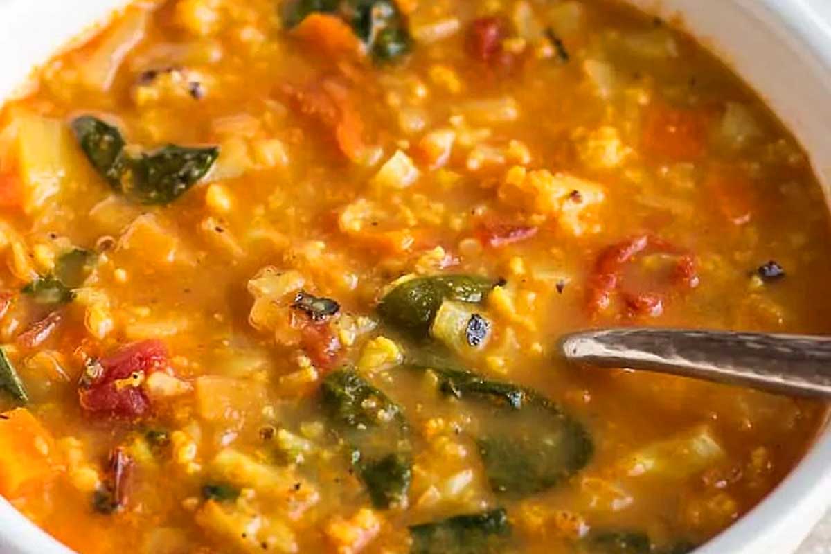 A bowl of tomato vegetable soup with a spoon.