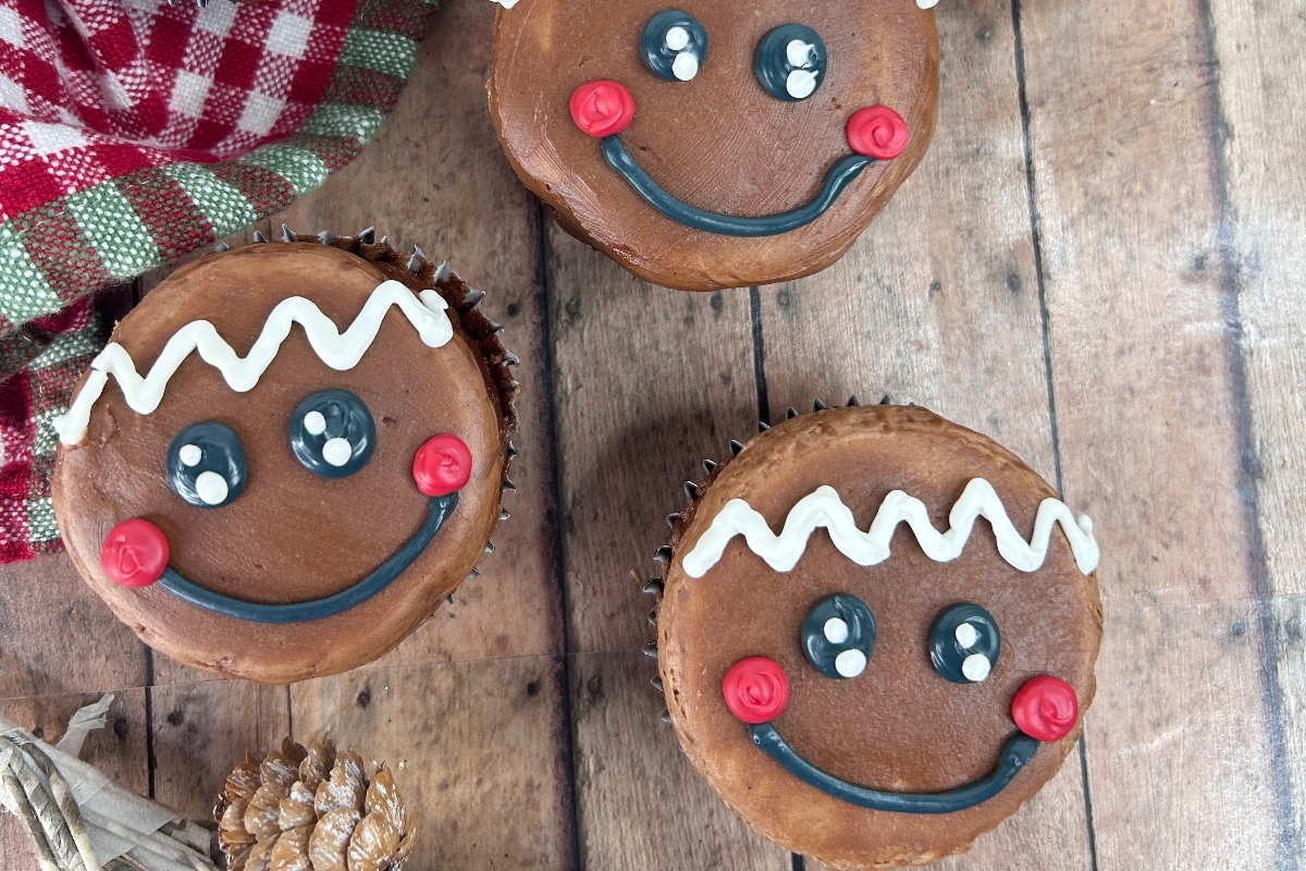 Three cute gingerbread cupcakes decorated with smiley faces and pine cones, perfect for Christmas.