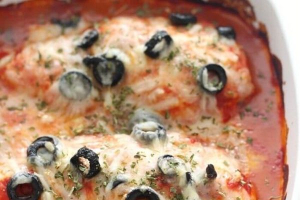 Chicken parmigiana in a casserole dish with olives and cheese.