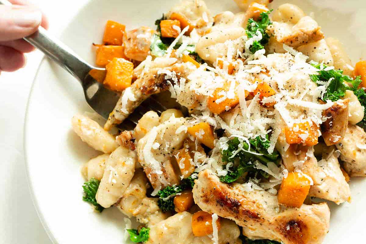 For a delightful date night, imagine a person holding a bowl of delectable pasta adorned with succulent chicken and vibrant kale.