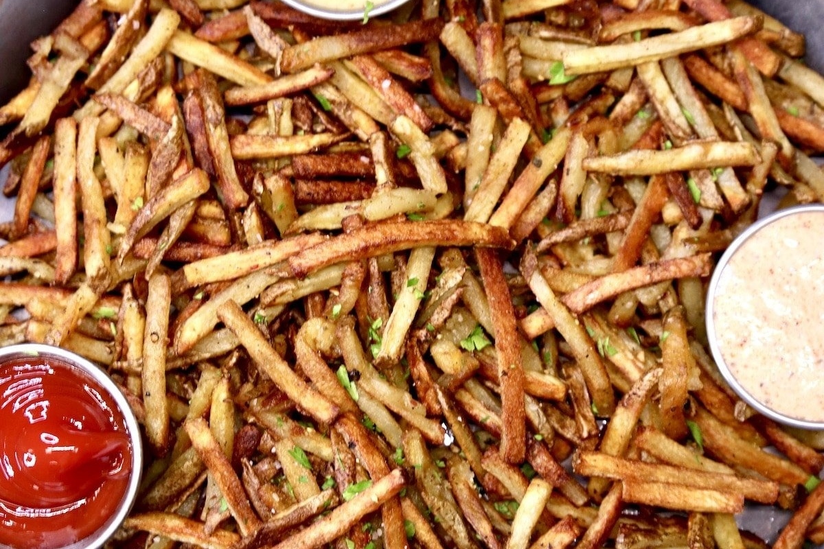 A plate of french fries with ketchup and dipping sauce, perfect for those looking for delicious fry recipes.
