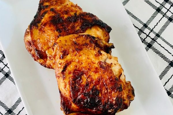 Two budget-friendly grilled chicken breasts on a white plate.