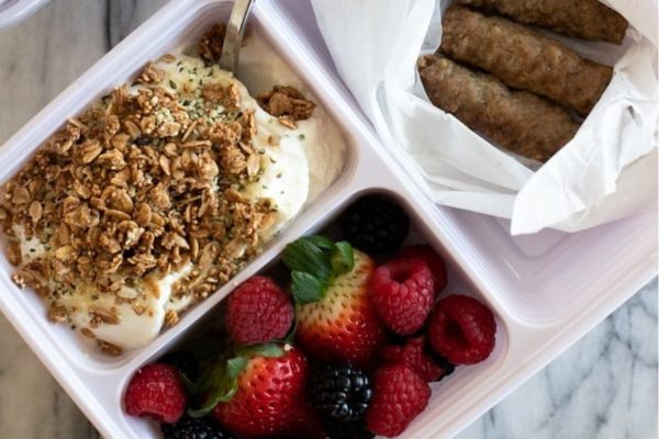 A breakfast lunch box with yogurt, granola, and fruit.