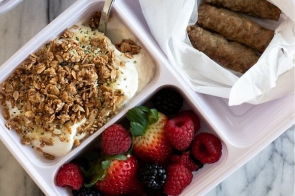 A lunch box with yogurt, granola and fruit.