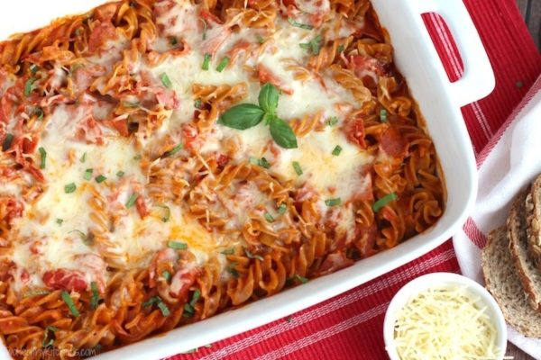 A casserole dish with pasta and bread on a red tablecloth.