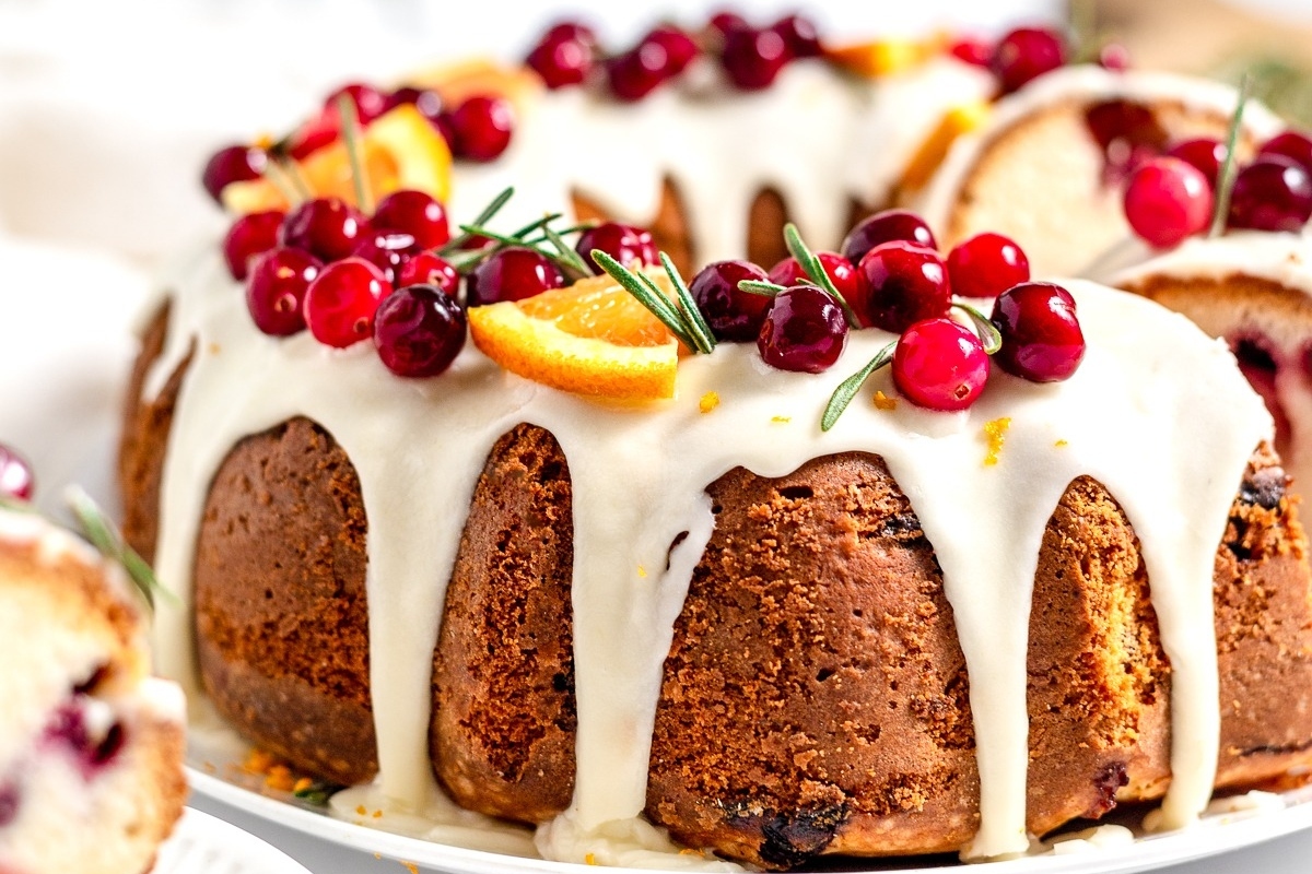A luscious bundt cake with cranberries and oranges on a plate.