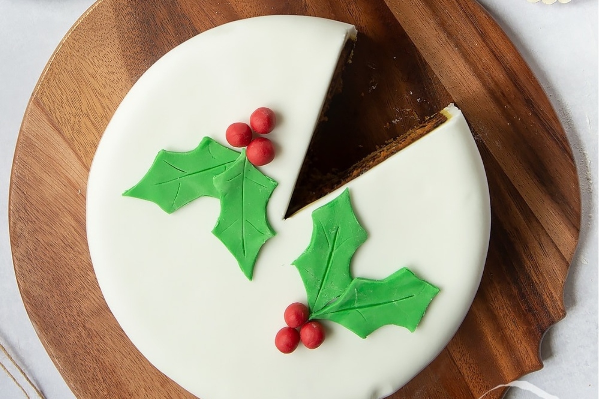 A Christmas cake adorned with holly leaves on a wooden board.