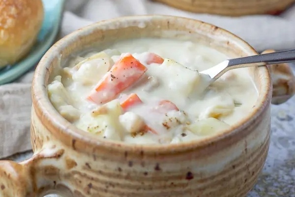 A bowl of chowder with carrots and potatoes.