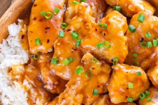 A bowl of asian chicken with rice and green onions.