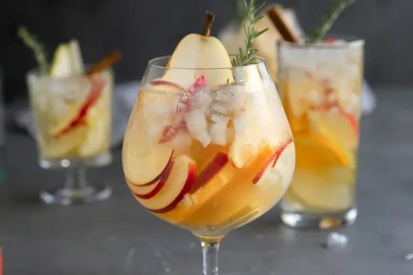 A glass of sangria with apples and sprigs of rosemary.