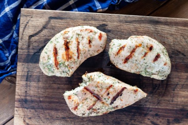 Three pieces of grilled chicken on a wooden cutting board.