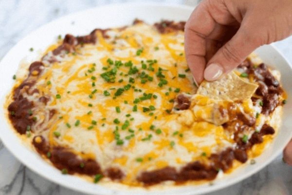 A person dipping a tortilla into a bowl of chili dip.