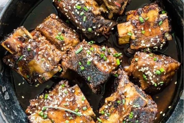 Ribs in a skillet with sauce and herbs.