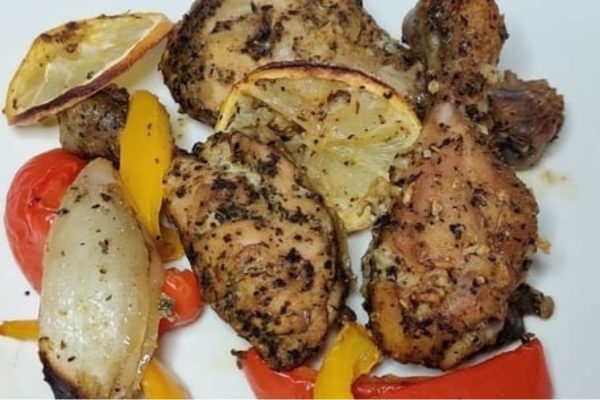 Roasted chicken with lemon and peppers on a white plate.