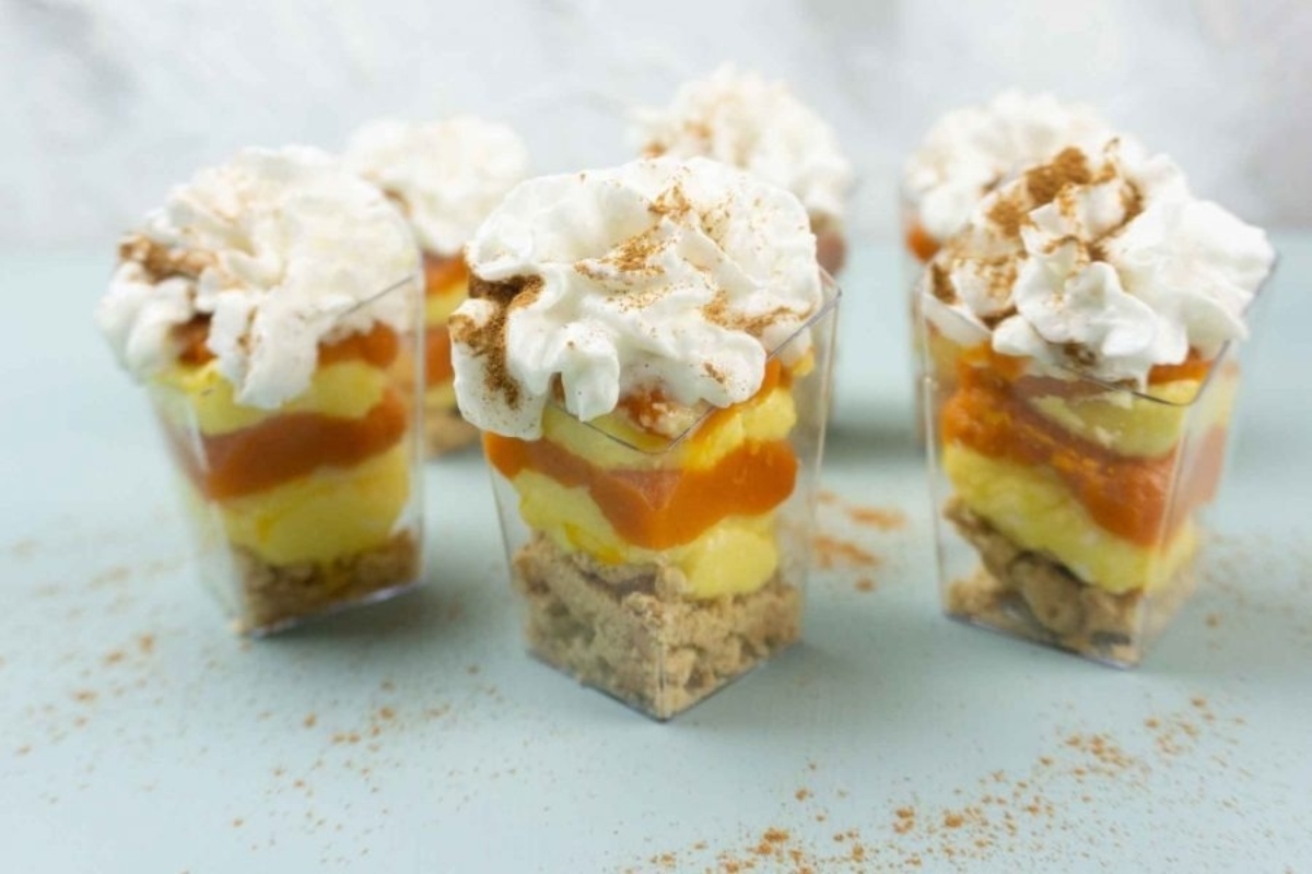A group of trifles in clear cups with whipped cream and granola.
