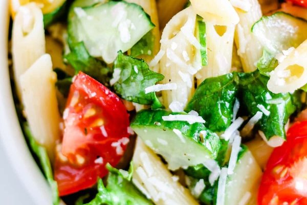 A bowl of penne pasta salad with tomatoes and cucumbers.