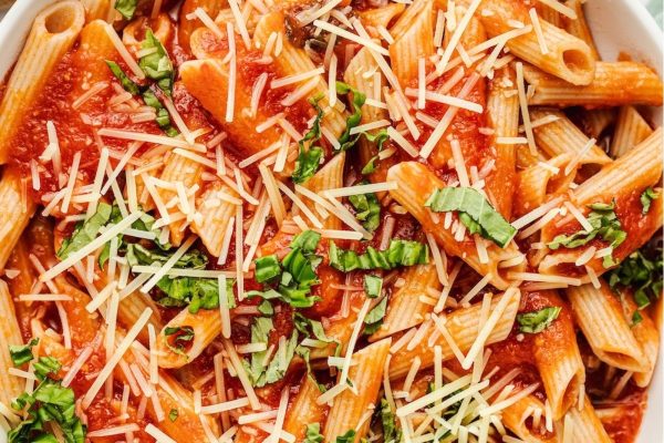 Delicious and creamy penne pasta served with a rich tomato sauce and topped with freshly grated parmesan cheese, all beautifully presented in a white bowl.