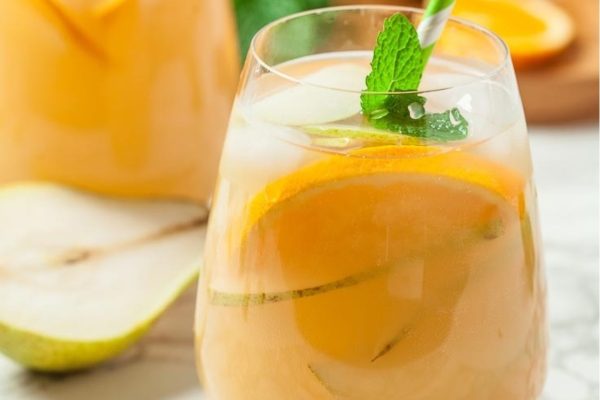 A glass of orange and pear sangria with mint leaves.