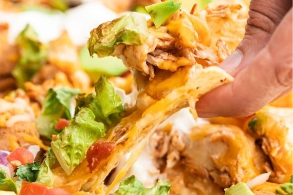A person grabbing a piece of chicken nachos.