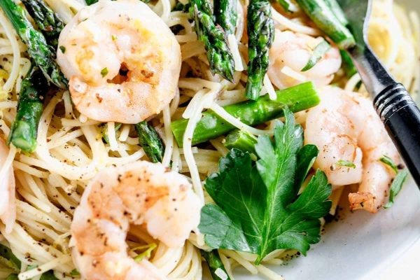 A bowl of pasta with shrimp and asparagus.